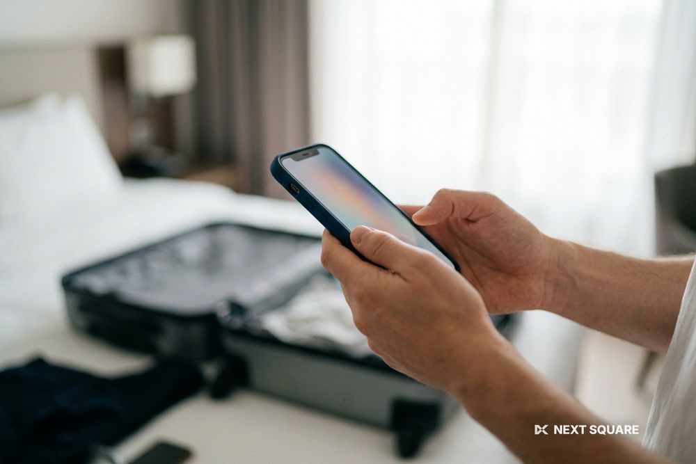 ホテルの部屋でスーツケースを広げ、スマートフォンを手に持つイメージ