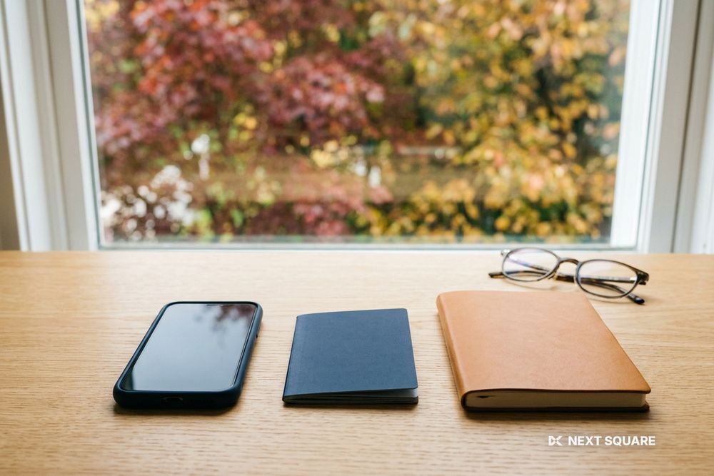 窓辺の机にスマートフォンとパスポート、ノートを置いたイメージ