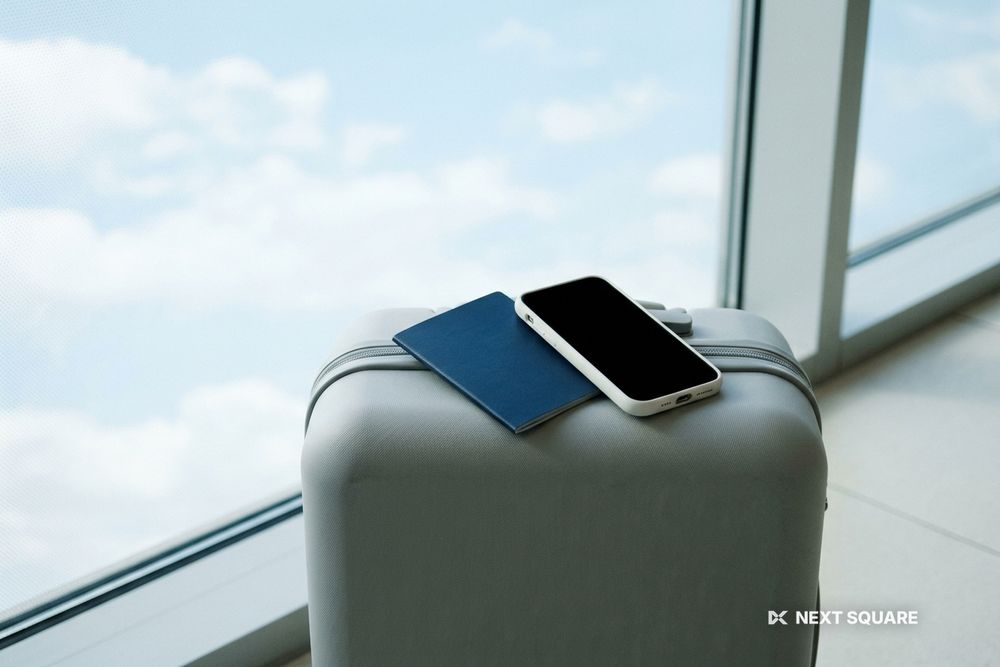 空港の窓辺でスーツケースの上に置いたパスポートとスマートフォンのイメージ