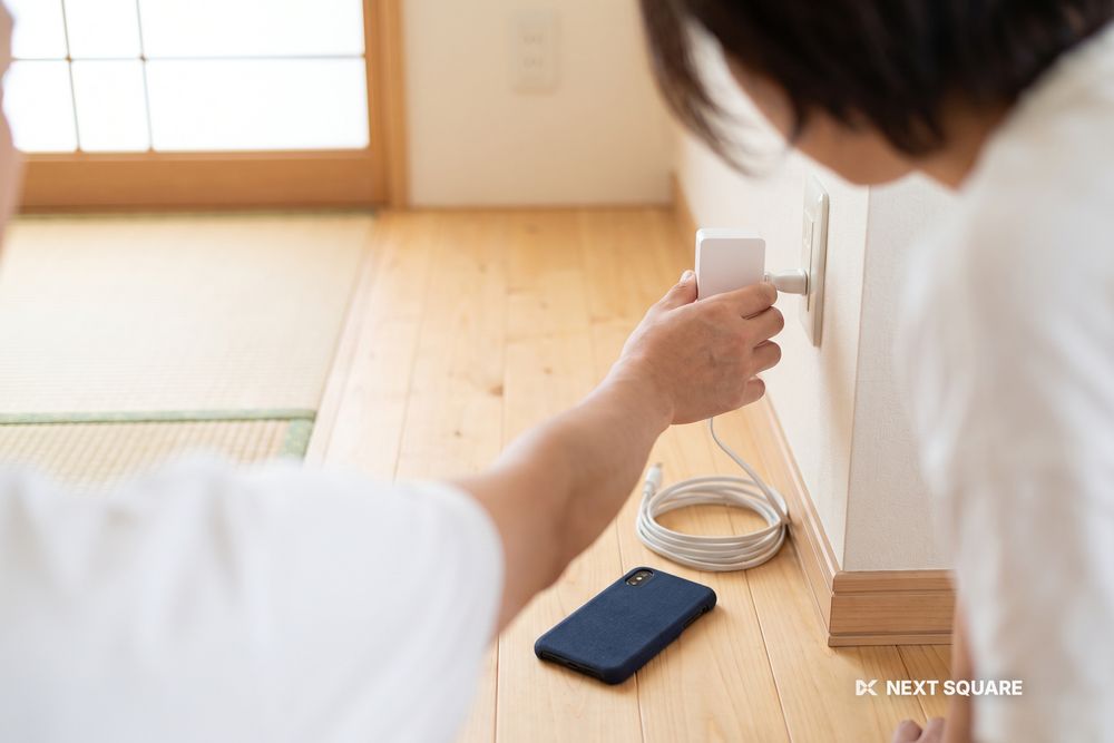 部屋の壁のコンセントに小型のホームルーターを挿し込もうとしている手元